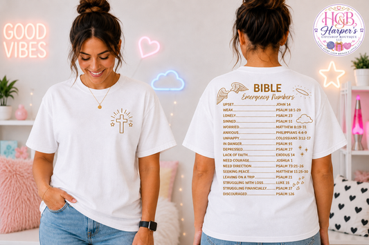 `White Bible Emergency Numbers t-shirt — front features gold cross design, back lists Bible verses for every emotional need — Christian faith gift by Harper's GiftShop Boutique`

**Front-facing shot:**
> `White Christian t-shirt with gold glowing cross and stars on left chest — faith-based apparel by Harper's GiftShop Boutique Fayetteville NC`

**Back-facing shot:**
> `Back of Bible Emergency Numbers shirt with angel wings graphic and list of scriptures for feeling upset, anxious, lonely, depressed, and mor